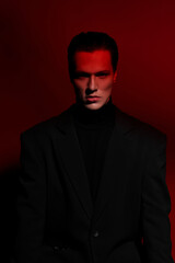 Close Up portrait of a handsome serious young man in black suit over red dark background. Horizontal view. Space for text.
