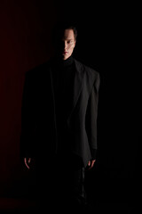 Fototapeta premium Close Up portrait of a handsome serious young man in black suit over red dark background. Horizontal view. Space for text.
