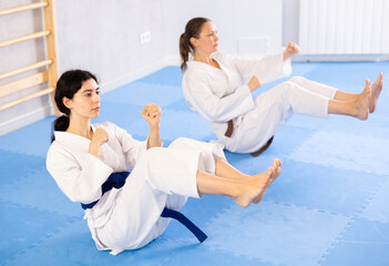 Adult woman and young woman in kimono doing abdominal exercises in gym