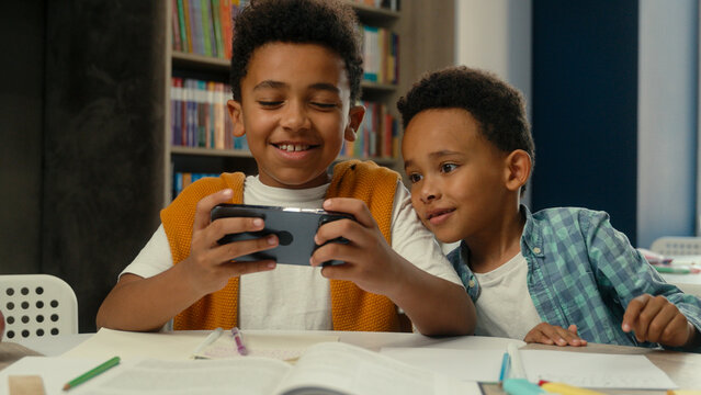Little boys African American siblings children school studying kids friends two brothers funny playing mobile phone game online together smartphone addict funny schoolboys students pupils gaming play - Powered by Adobe