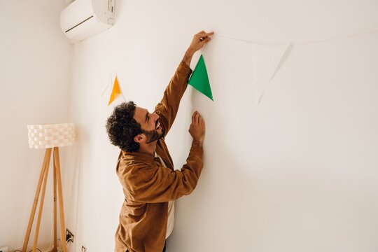 Man standing and laughing while hanging ribbon on wall, in apartment, preparing for birthday party