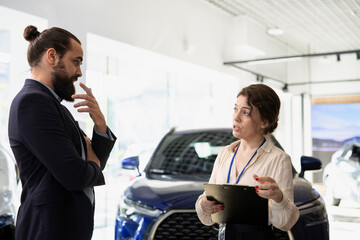 Woman working in dealership answering customers questions about cars, financing and purchase...