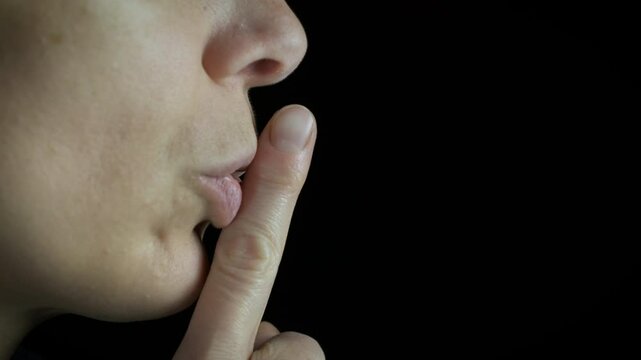 Lady keep quiet gesture on black background. A view of woman keep silence and put the finger by the mouth on the black background.