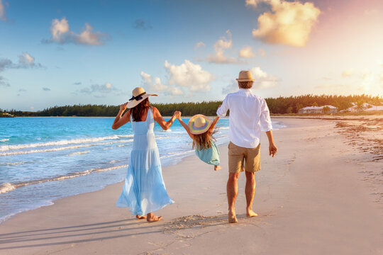 A happy family in walks hand in hand down a tropical beach during sunset tme and enjoys their summer vacation time