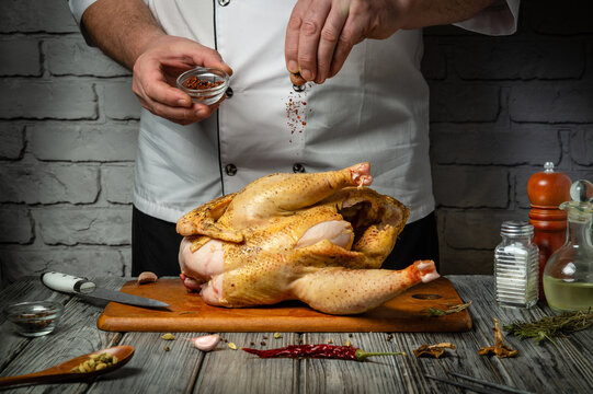 A skilled chef delicately seasons a whole broiler chicken with spices in a warmly lit kitchen, showcasing the art of cooking. Asian cuisine