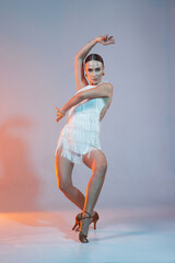 Elegant female Latin dancer in a white fringed dress performing a dynamic move with grace and...
