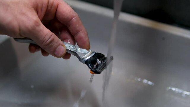 Cleaning shaving razor in bathroom sink. Rinsing off razor with water.