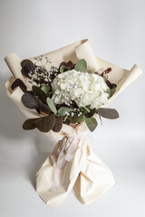 Elegant white hydrangea bouquet wrapped in soft paper with accents of greenery and delicate white...