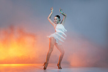 Obraz premium Elegant female Latin dancer in a white fringed dress performing a dynamic move with grace and confidence in artistic lighting.