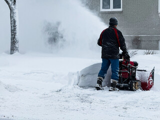 Homme nettoyant la neige de l'allée avec une souffleuse à neige un jour d'hiver