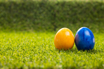 Two Easter eggs blue and yellow on a green lawn stand on the right