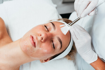 Professional beautician applying glycolic acid peel on face of beautiful young woman. Chemical peeling and beauty treatment concept.