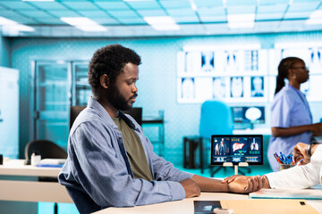 African american medic monitoring pulse and heartbeat with a smartwatch for a patient, looking at...