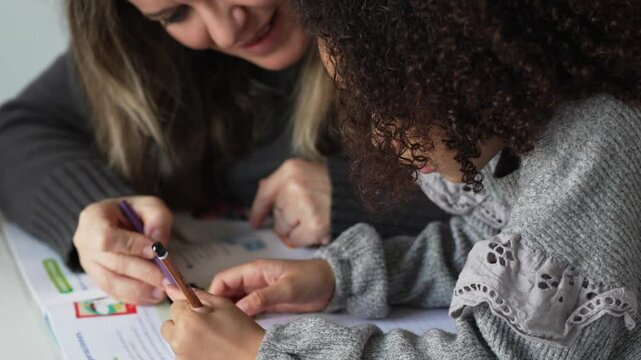 Caucasian mother and African American daughter studying at home, doing homework in cosy white room. Parent teach, child school girl learn knowledge, write exercise read book. Education for children
