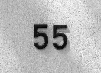 Street address number, number 55. Black metal address numbers on a white stucco wall.
