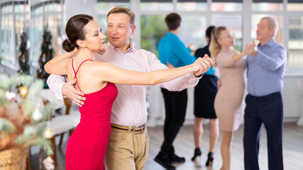 Men and women dancing tango or samba next to the Christmas tree