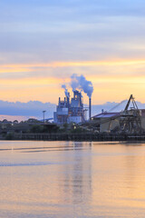Fototapeta premium An expansive factory complex illuminated by the golden glow of a tropical sunset, surrounded by dense forest, June 25, 2019, highlighting industry coexisting with wild nature, location unspecified