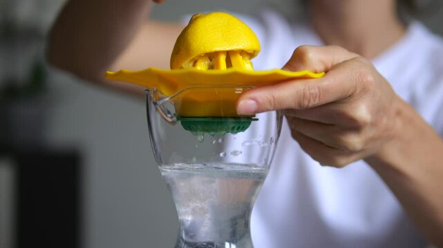 Female hands squeezing ripe yellow lemon with citrus reamer, extracting fresh juice into transparent glass carafe, preparing natural hydrating beverage. concept obtaining freshly squeezed lemon juice