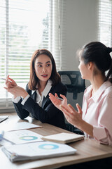 Two women engaged in a business meeting, analyzing charts and data in a well-lit office environment.