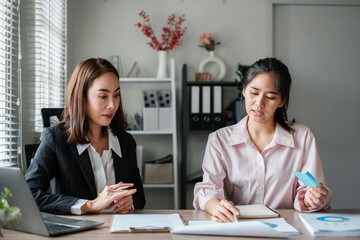Fototapeta premium Two women in a modern office setting discussing business documents at a desk, showcasing teamwork and collaboration.