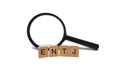 Wooden blocks with ENTJ letters, and a magnifying glass. ENTJ is one of the 16 personality types identified by the Myers-Briggs Type Indicator or MBTI. Concept of psychology.