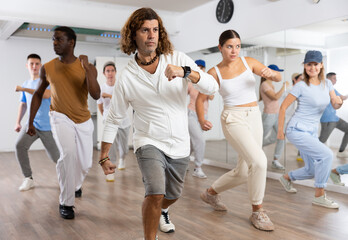 Class of active young adult dancers performing steps during exercising modern dance together in dance hall