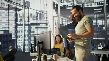 Cheerful admin holding laptop chatting with colleagues while working with machine learning tech....