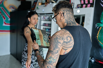 Professional tattoo artist showing tattoo design to customer on digital tablet in a modern studio