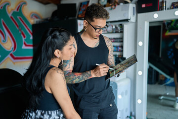 Professional tattoo artist reviewing design on digital tablet with client inside modern studio