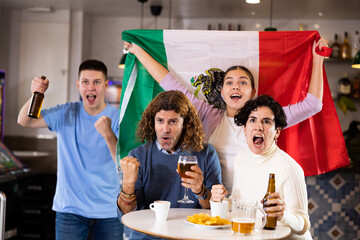 Company of emotional young adult sports fans supporting Mexican team with state flag while resting in pub with beer