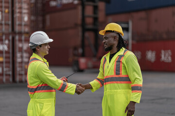 Two professional workers in neon reflective suits shake hands in a logistics hub, highlighting teamwork, agreement, and successful coordination in freight, transportation, and supply chain operations