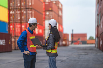 Two logistics workers man and woman discuss operations at a busy shipping container yard.