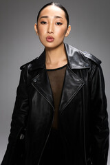 Fototapeta premium Fashion asian woman in black leather jacket striking a pose with hand on hip for camera