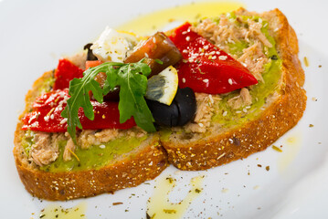 Healthy toasts with guacamole, canned tuna, feta cheese, fresh vegetables and lemon served on white plate..