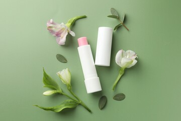 Lip balm and freesia flowers on light green background, flat lay