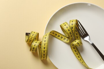 Bulimia. Plate with fork and measuring tape on beige background, top view