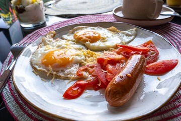 English breakfast in a restaurant, scrambled eggs and sausage with tomato on a plate on the table.