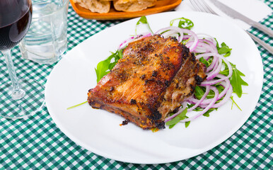 Baked pork ribs baked served at plate with salad from arugula and onion