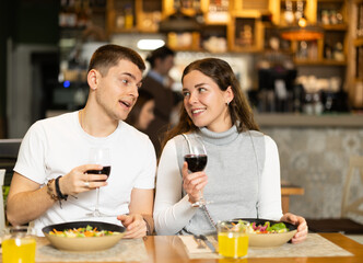 Girl spends time with guy in cafe, they chat and joke, eating and drinking wine. Date, romantic meeting, nice time together. Atmosphere of cafe, restaurant conducive to communication.