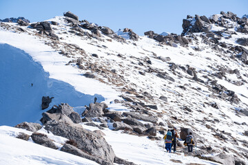 A group of women with backpacks move along a mountain ridge towards the summit, Climbing Kumbel Peak in winter. Tourists in the mountains near Almaty, Kazakhstan.