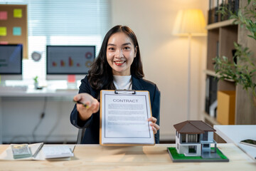 A woman is holding a contract in front of a house model