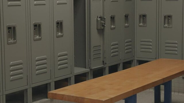 A slow panning shot moves from left to right, capturing a row of metal lockers and a wooden bench in a locker room. The scene emphasizes symmetry and a clean, structured layout.