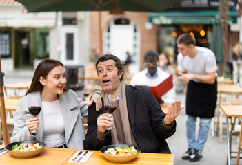 Girl spends time with man in cafe, they chat and joke, eating and drinking wine. Date, romantic meeting, nice time together. Atmosphere of cafe, restaurant conducive to communication.