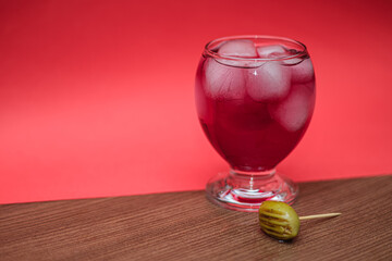 Chilled berry drink with ice. A decorative skewer with an olive adds an elegant touch to the presentation. Selective focus.
