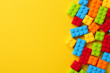 Constructor toy. Many colorful building blocks on yellow background, flat lay. Space for text