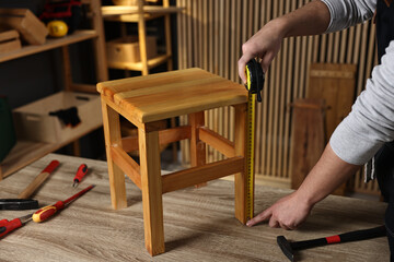 Repairman measuring wooden stool at table in workshop, closeup