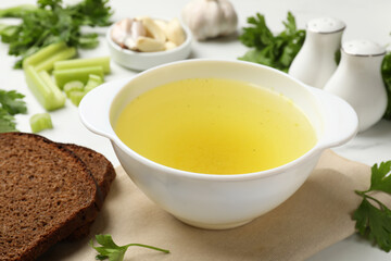 Tasty chicken bouillon in bowl with bread and ingredients on white table, closeup