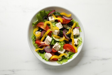 Delicious fresh Greek salad in bowl on white marble table, top view