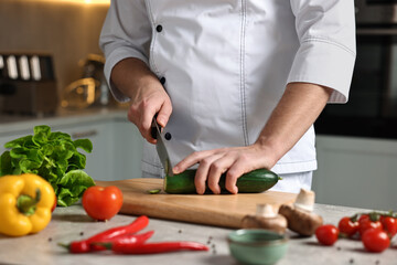 Professional chef cutting zucchini at table in kitchen, closeup