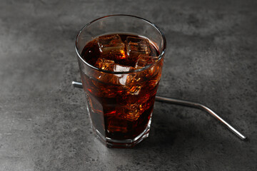 Cold cola with ice cubes in glass and drinking straw on grey table, closeup